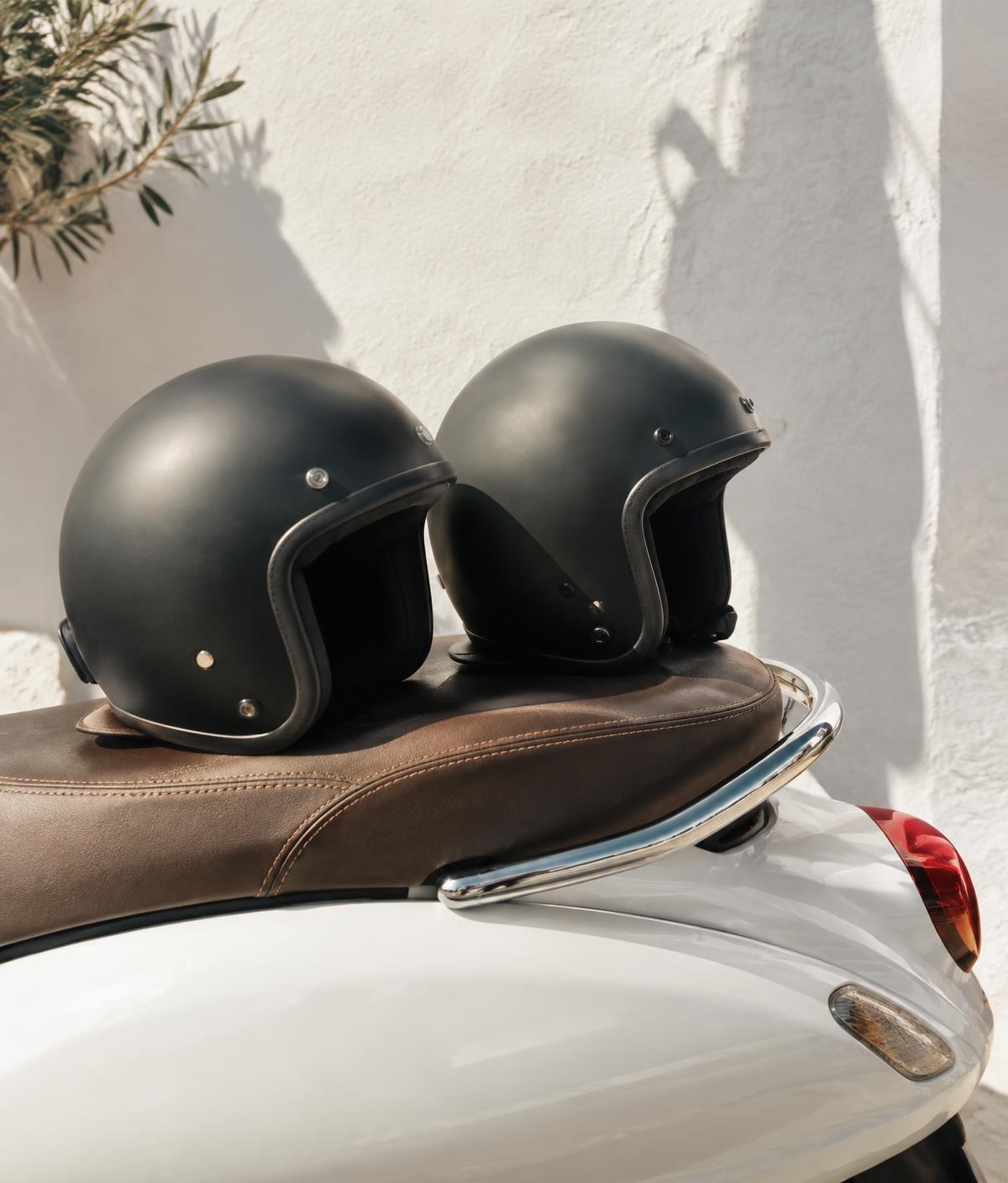 Two helmets on a scooter seat against a whitewashed wall